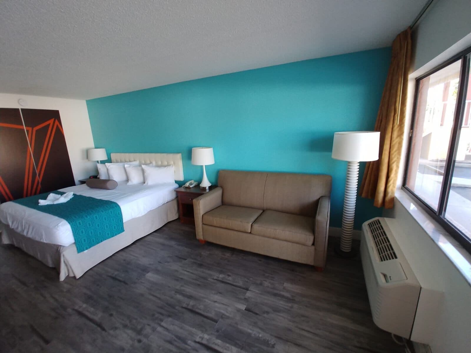 A hotel room with a bed, a sofa, a desk, and a window with curtains.