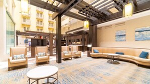 A spacious lobby with a high ceiling, a central seating area with sofas and armchairs, a round table, and a bookshelf. - Doubletree Suites by Hilton at The Battery Atlanta (Atlanta)