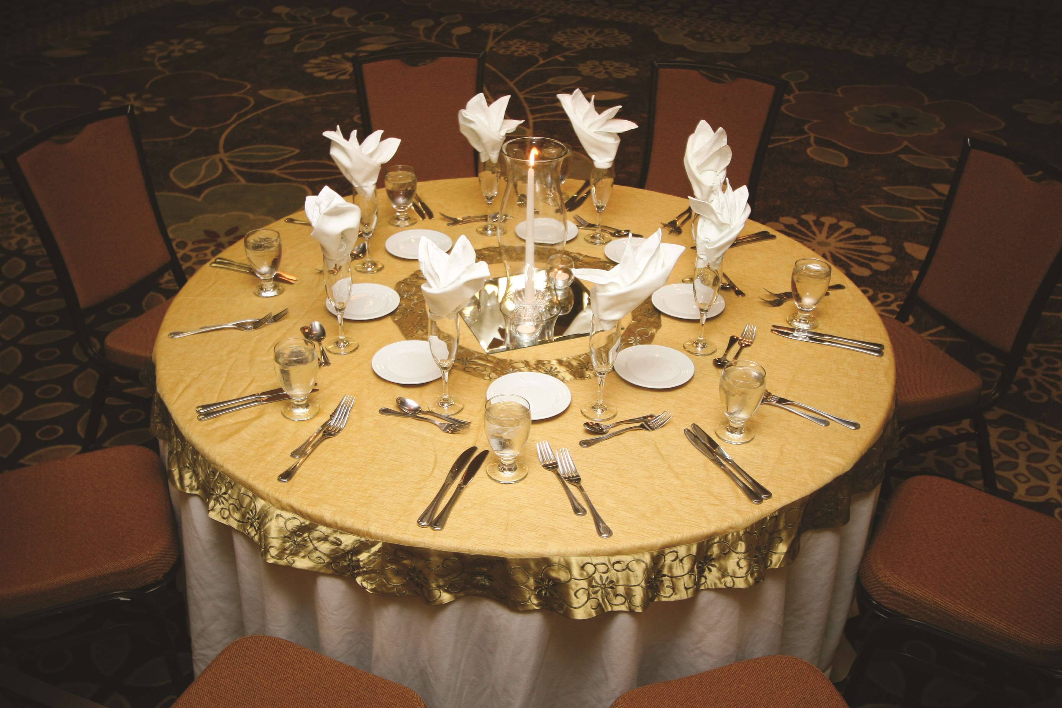 A round table set for a formal dinner with white napkins, silverware, and a lit candle centerpiece.