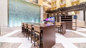 A modern hotel lobby with a bar area, seating, a large screen TV, and a decorative wall. - Doubletree Suites by Hilton at The Battery Atlanta (Atlanta)