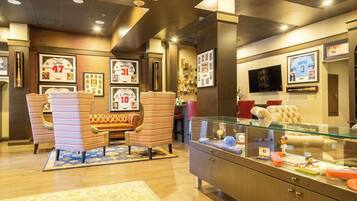 Un vestíbulo de hotel con sillones a rayas, un sofá, camisetas deportivas enmarcadas, una vitrina de cristal con figuritas y un televisor en la pared.