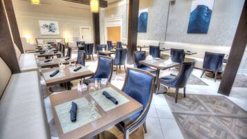 A hotel dining area with multiple tables and chairs, arranged in a spacious layout.
