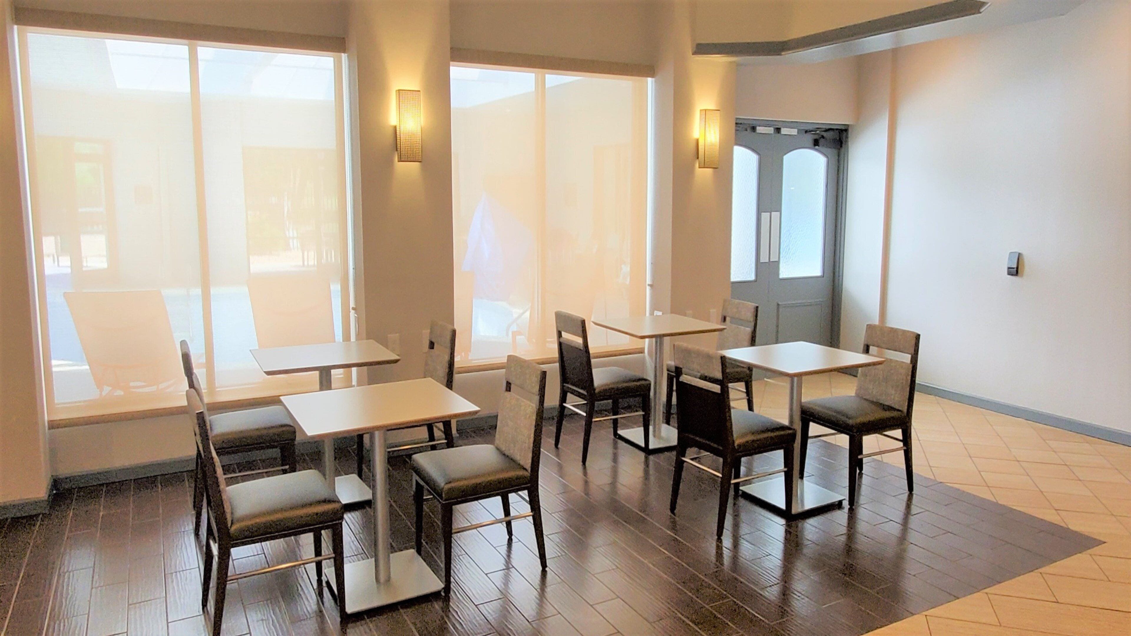 A dining area with tables and chairs, large windows, and wall-mounted lighting.