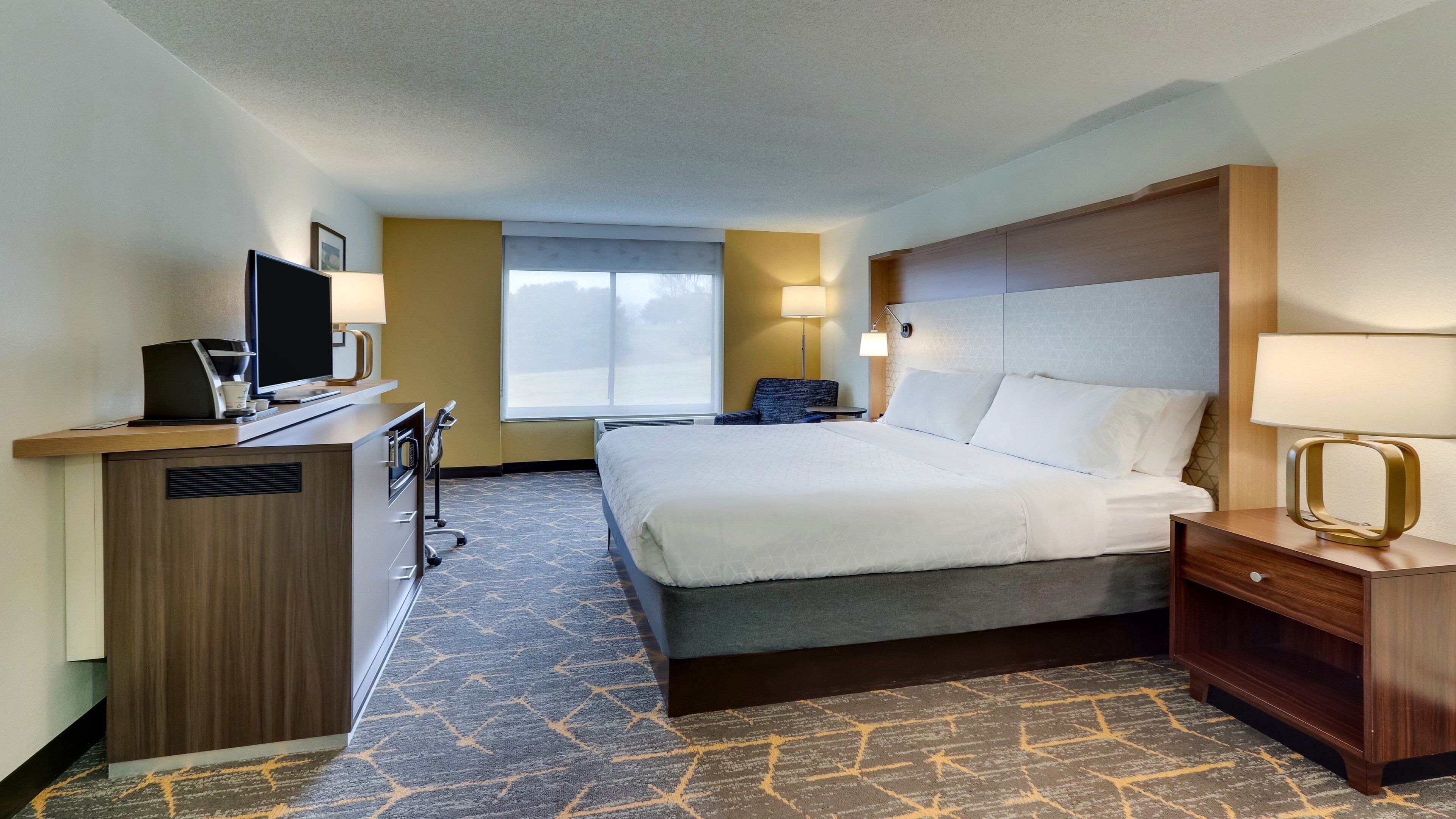 Une chambre d’hôtel avec un lit, un bureau, une chaise et une fenêtre.