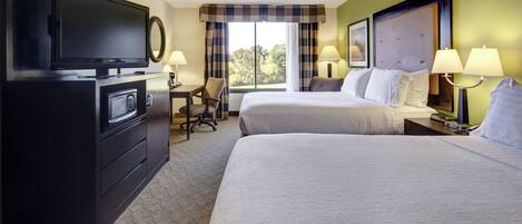 A hotel room with a television, a desk, two beds, and a window with curtains.