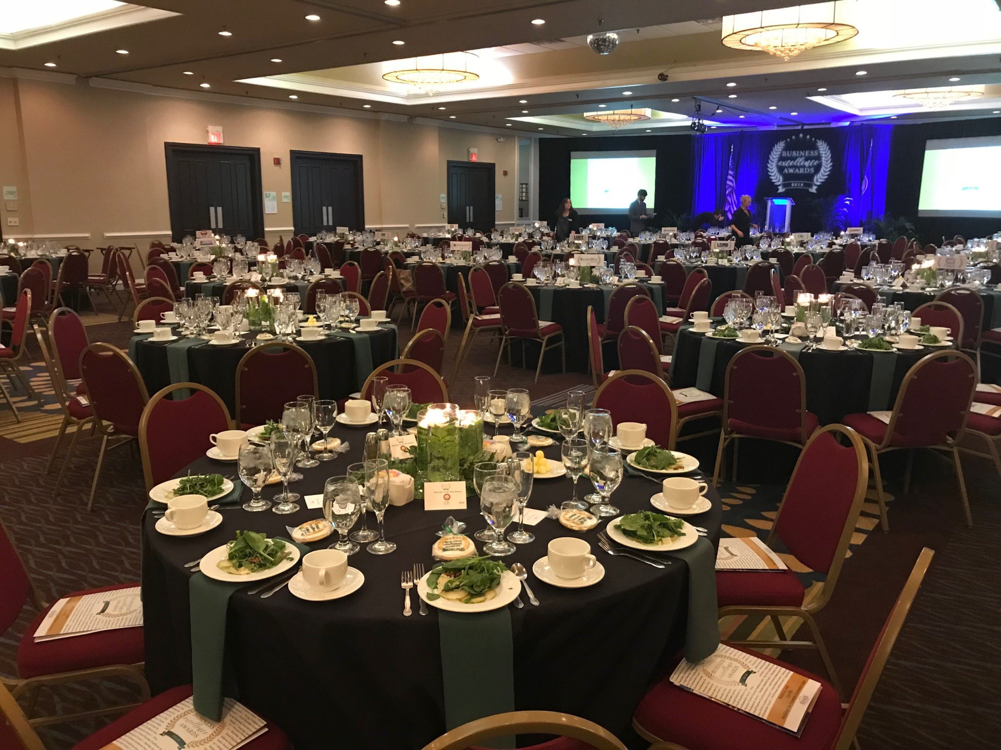 Une salle de banquet avec des tables rondes dressées pour un événement formel, agrémentées de marque-places et de couverts.