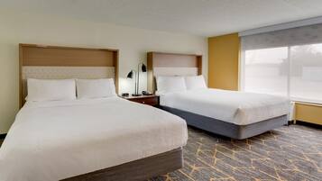 A hotel room with two beds, a nightstand with a lamp, and a large window.