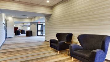 A hotel lobby with striped carpet, two armchairs, a small table, and a reception desk in the background.