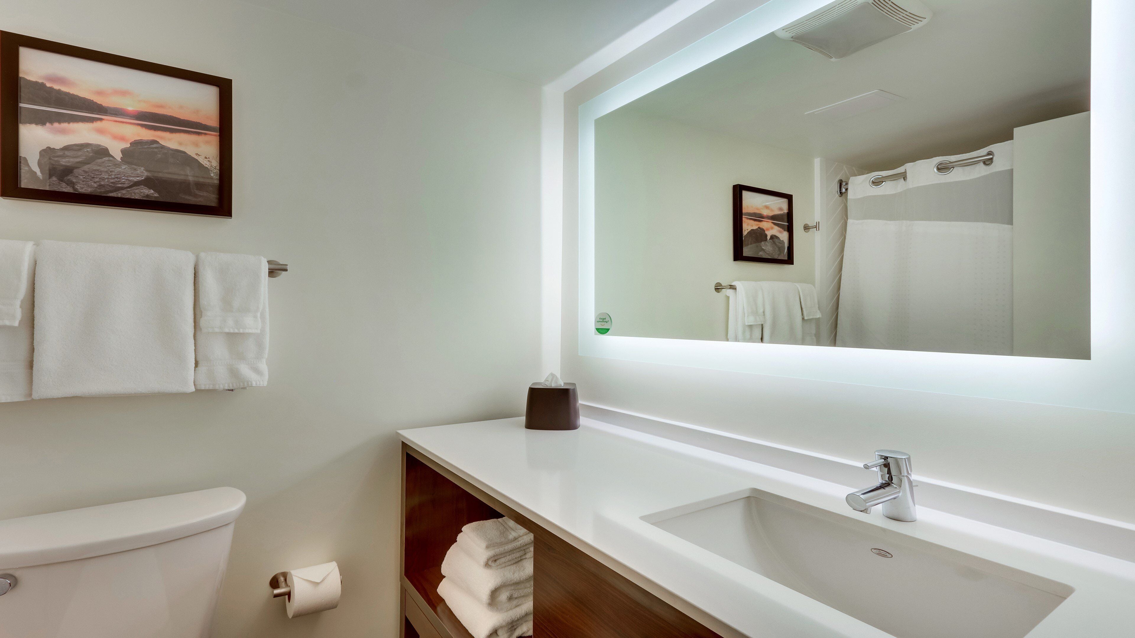 A modern bathroom with a large mirror, white sink, and toilet.