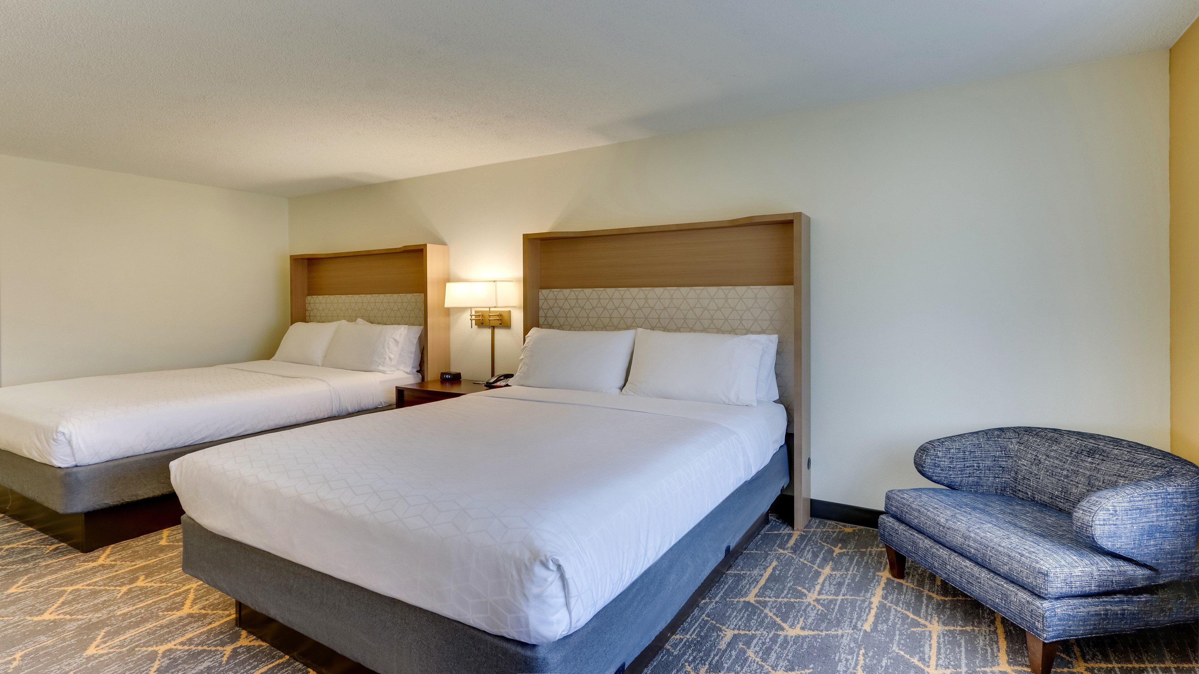 A hotel room with two beds, a chair, and a nightstand with a lamp.