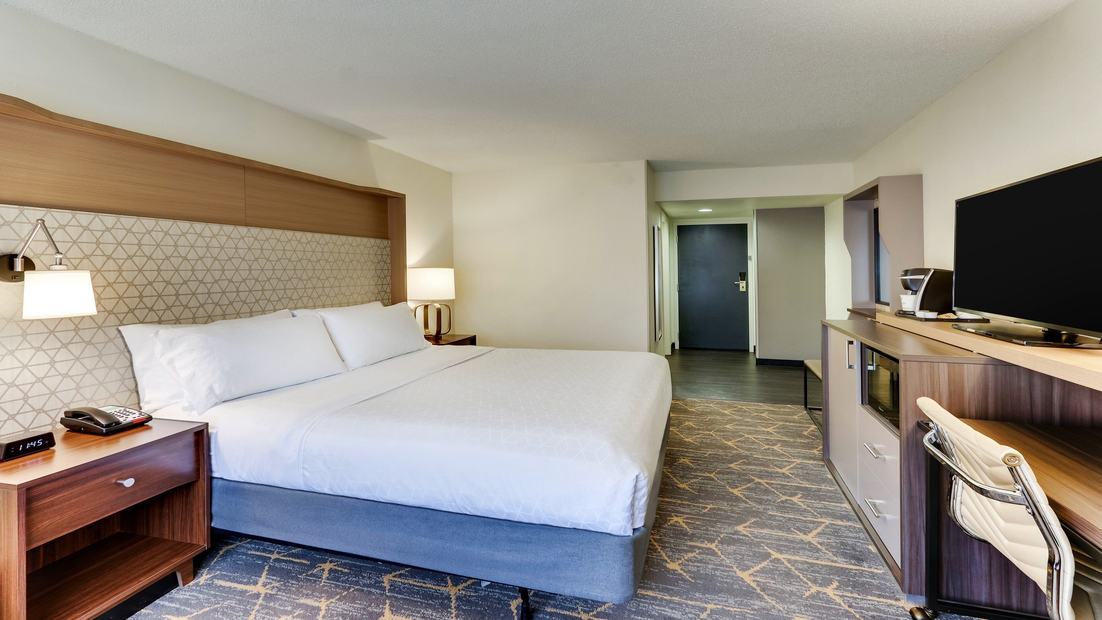 A hotel room with a bed, bedside tables, a TV, and a desk.