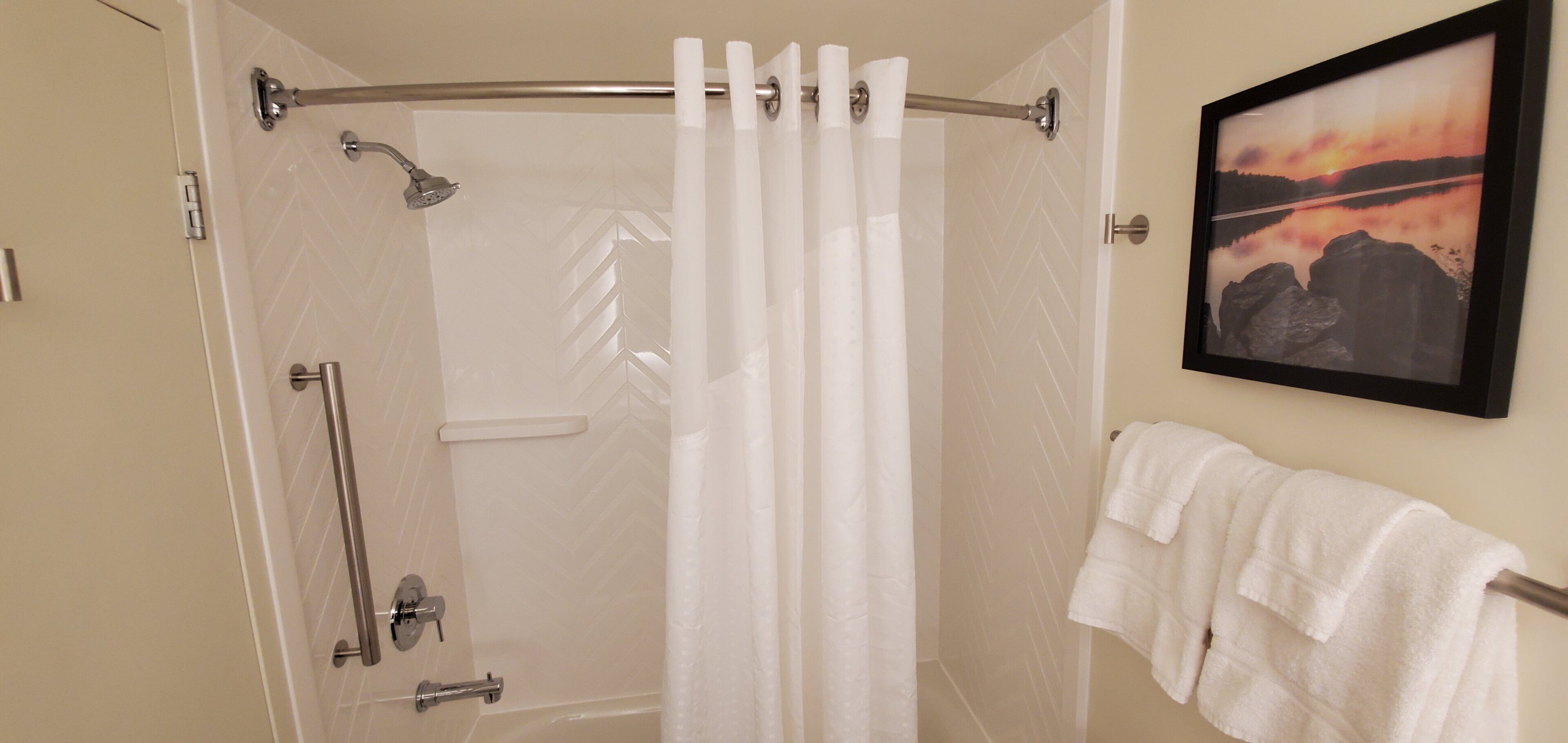 A shower with a glass door, a handrail, and a towel rack with a white towel.