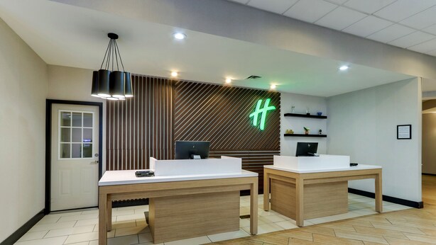 A reception area with two wooden desks, a modern light fixture, and a wall-mounted sign. - Holiday Inn Staunton Conference Center by IHG (Staunton)