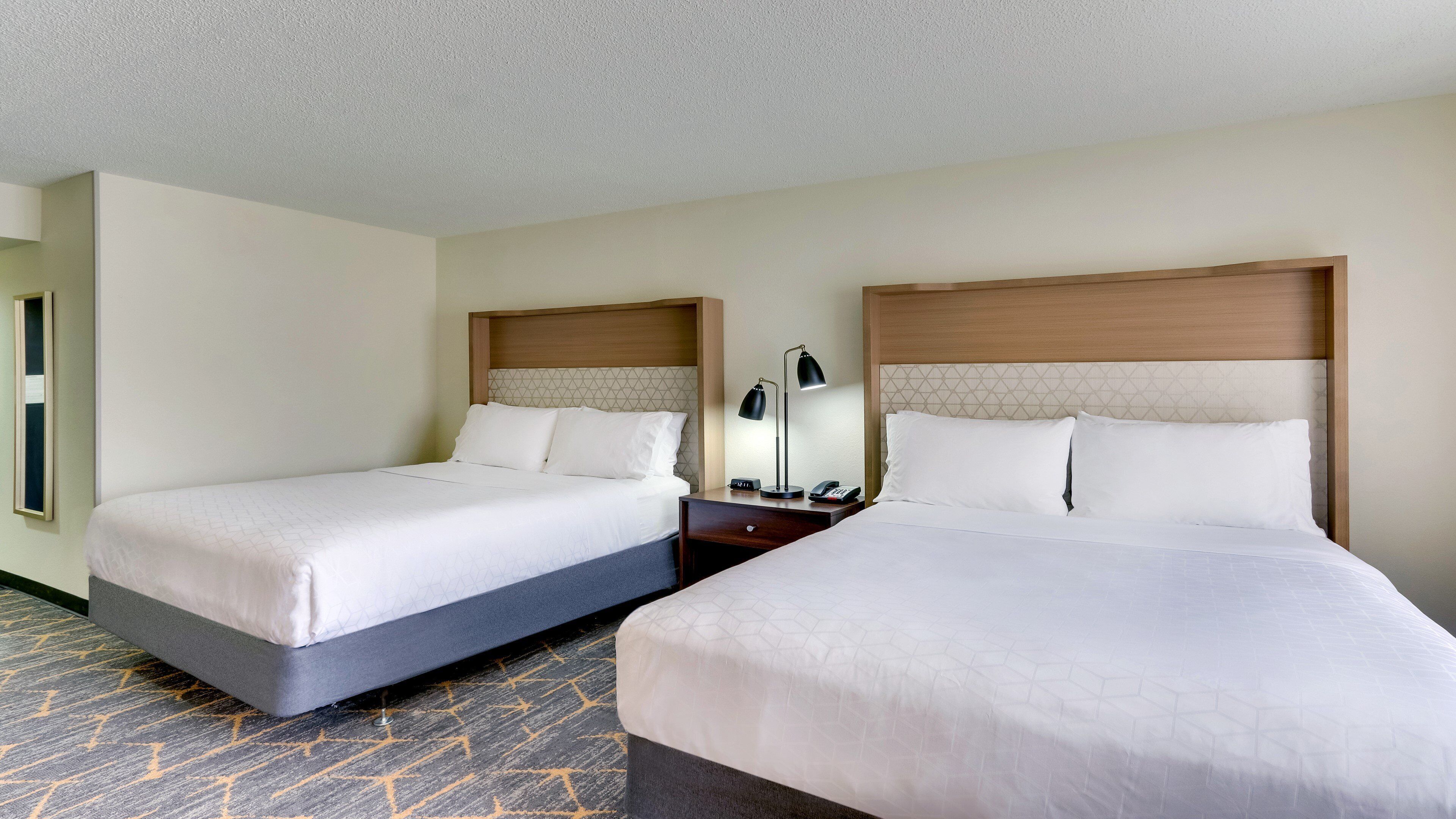 A hotel room with two beds, a nightstand with a lamp, and a clock.