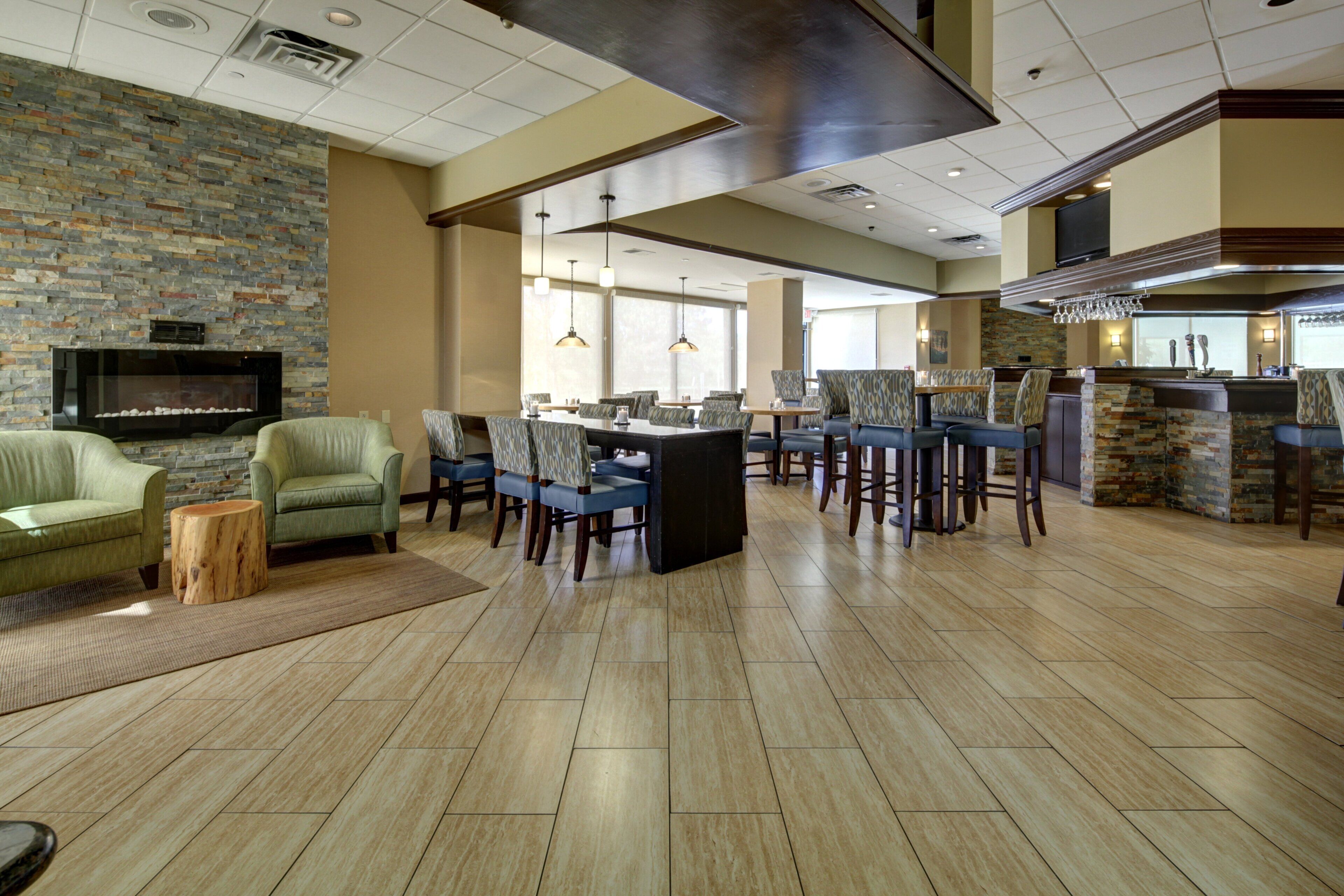A spacious hotel lobby with a stone fireplace, comfortable seating, a bar area, and a large television.