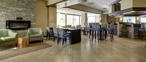 A spacious hotel lobby with a stone fireplace, comfortable seating, a bar area, and a large television.