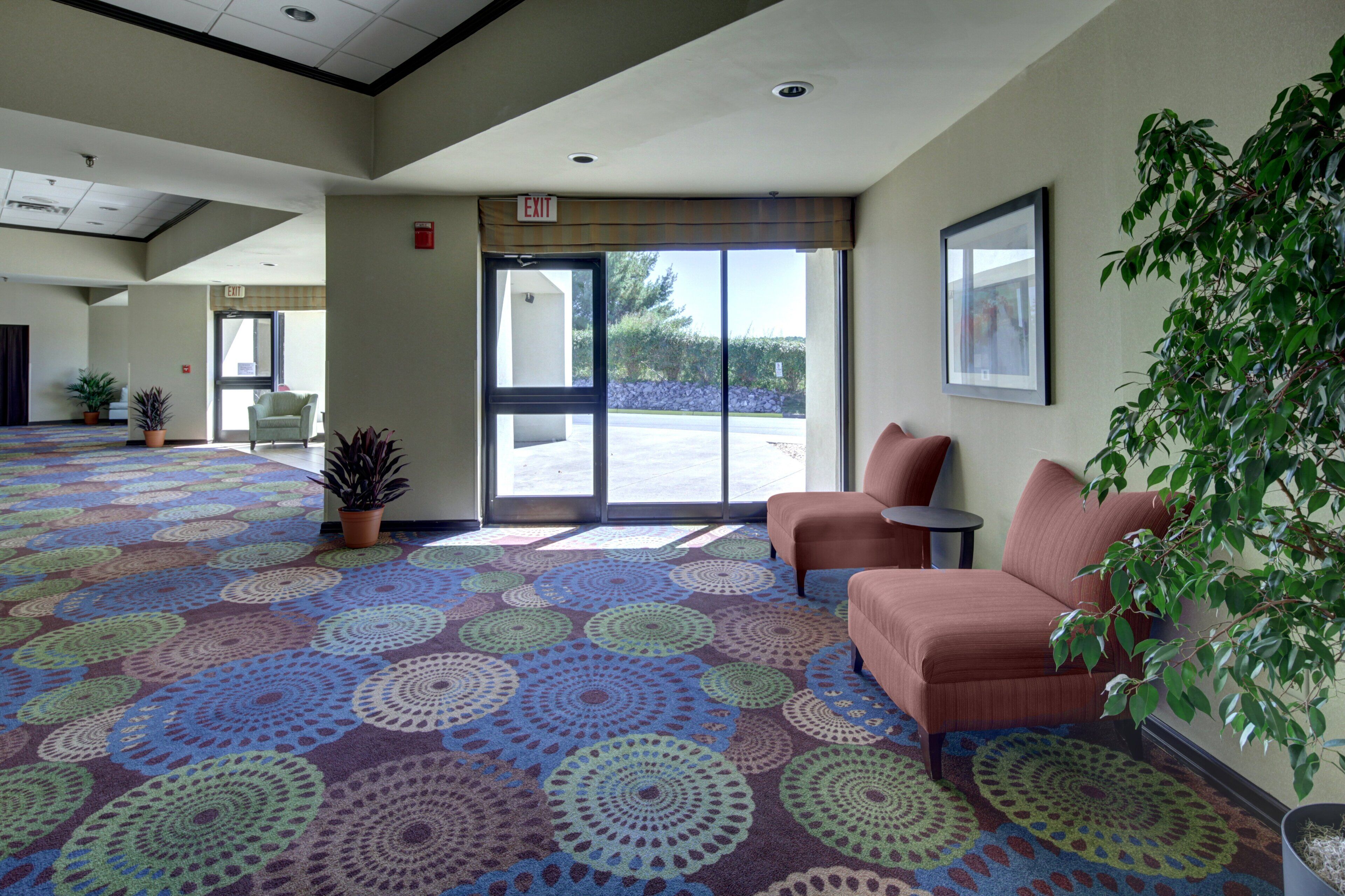 A hotel lobby with a patterned carpet, two sofas, a potted plant, and a framed picture on the wall.