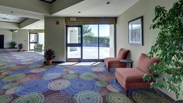 A hotel lobby with a patterned carpet, two sofas, a potted plant, and a framed picture on the wall.
