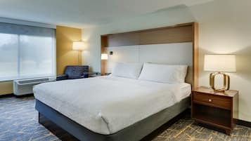 Una habitación de hotel con una cama grande, una silla, una mesita de noche, una lámpara y un calentador.