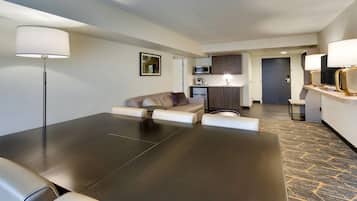 Een moderne hotelkamer met een donker houten tafel, een beige bank, een klein rond tafeltje en een kitchenette op de achtergrond.