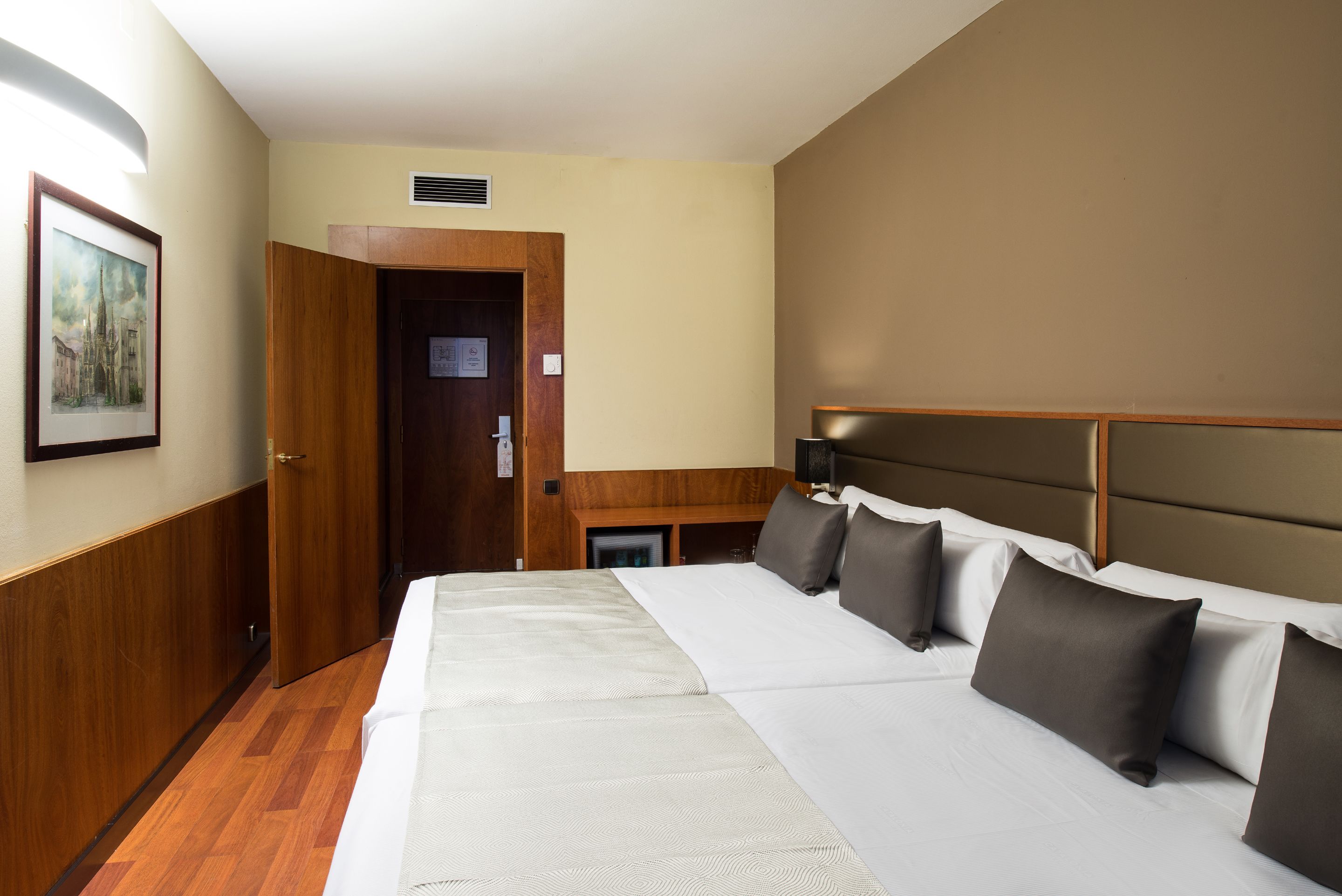 A hotel room with a large bed, a wooden door, a small desk, and a framed picture on the wall.