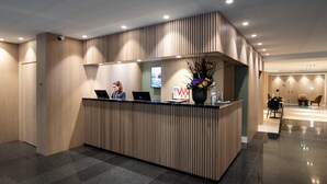 A reception desk with a modern design, a flat-screen TV, and a vase with flowers. - Catalonia Diagonal Centro (Barcelona)