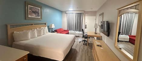 A hotel room with a large bed, a desk with a chair, a television, and a wardrobe.