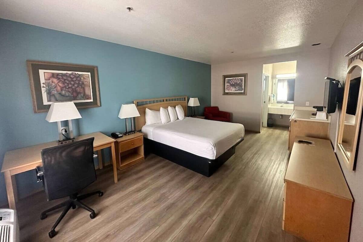 A hotel room with a bed, desk, chair, and a mirror.