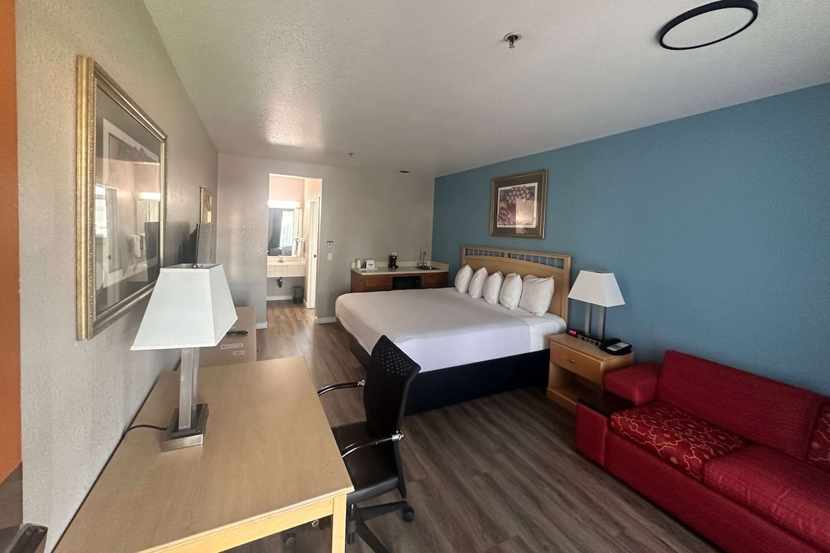 A hotel room with a bed, a desk, a red sofa, a nightstand, and a mirror.