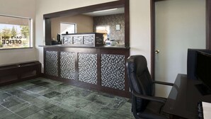 Un área de recepción con un mostrador de madera oscura, una computadora y una zona de estar con una silla.