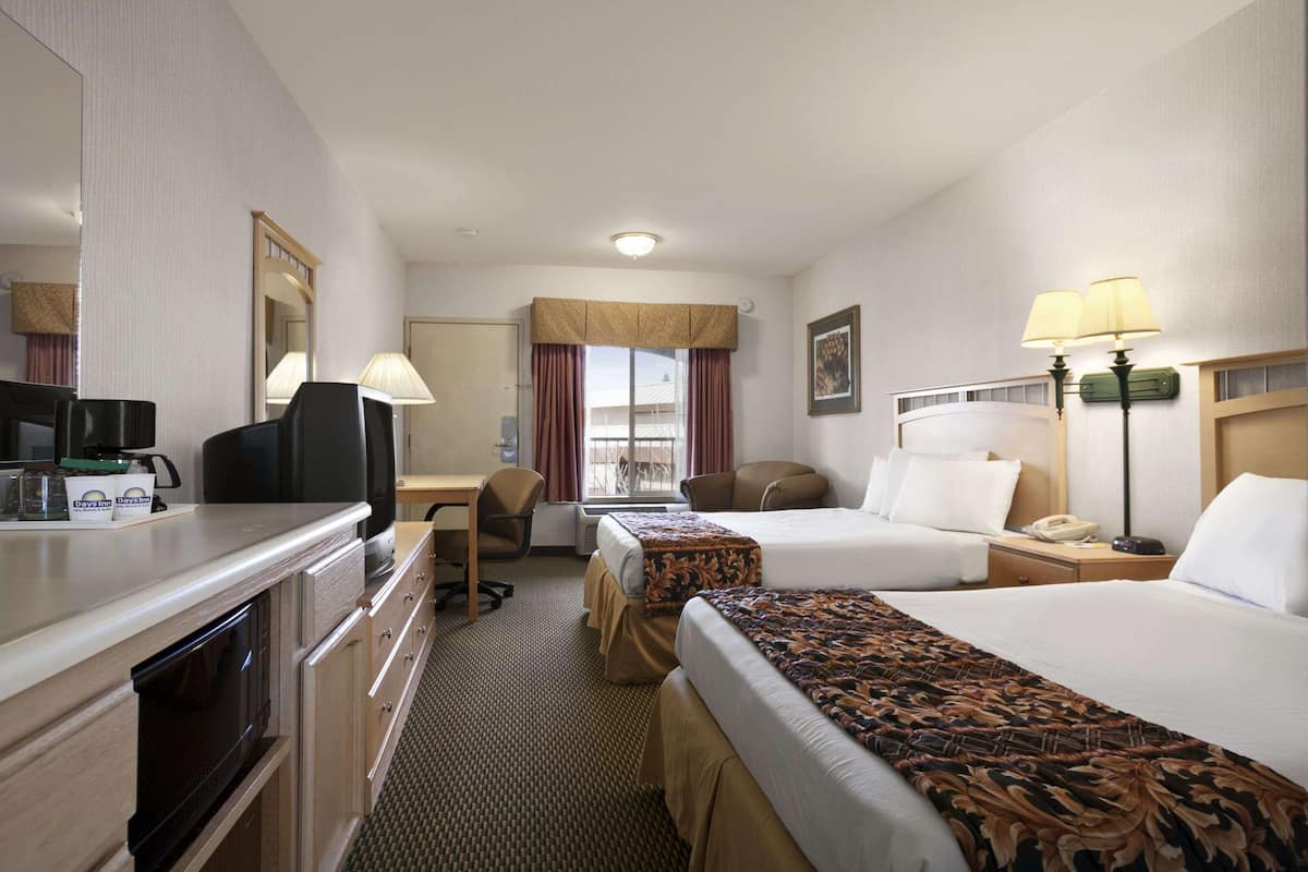 A hotel room with a desk, two beds, a microwave, a coffee maker, and a window with curtains.