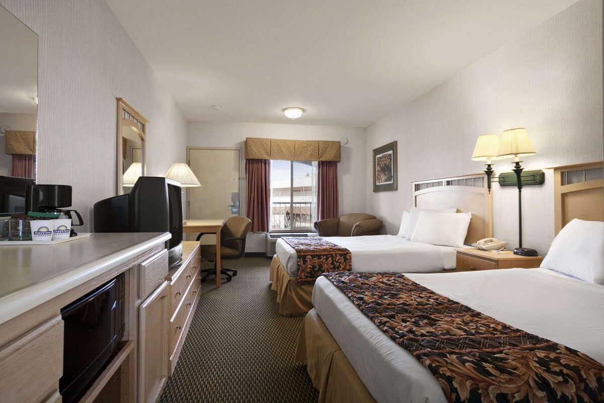 A hotel room with a desk, two beds, a microwave, a coffee maker, and a window with curtains.