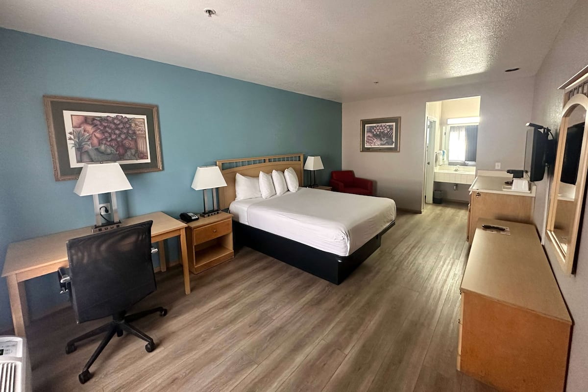 A hotel room with a bed, desk, chair, bedside tables, lamps, and a mirror.