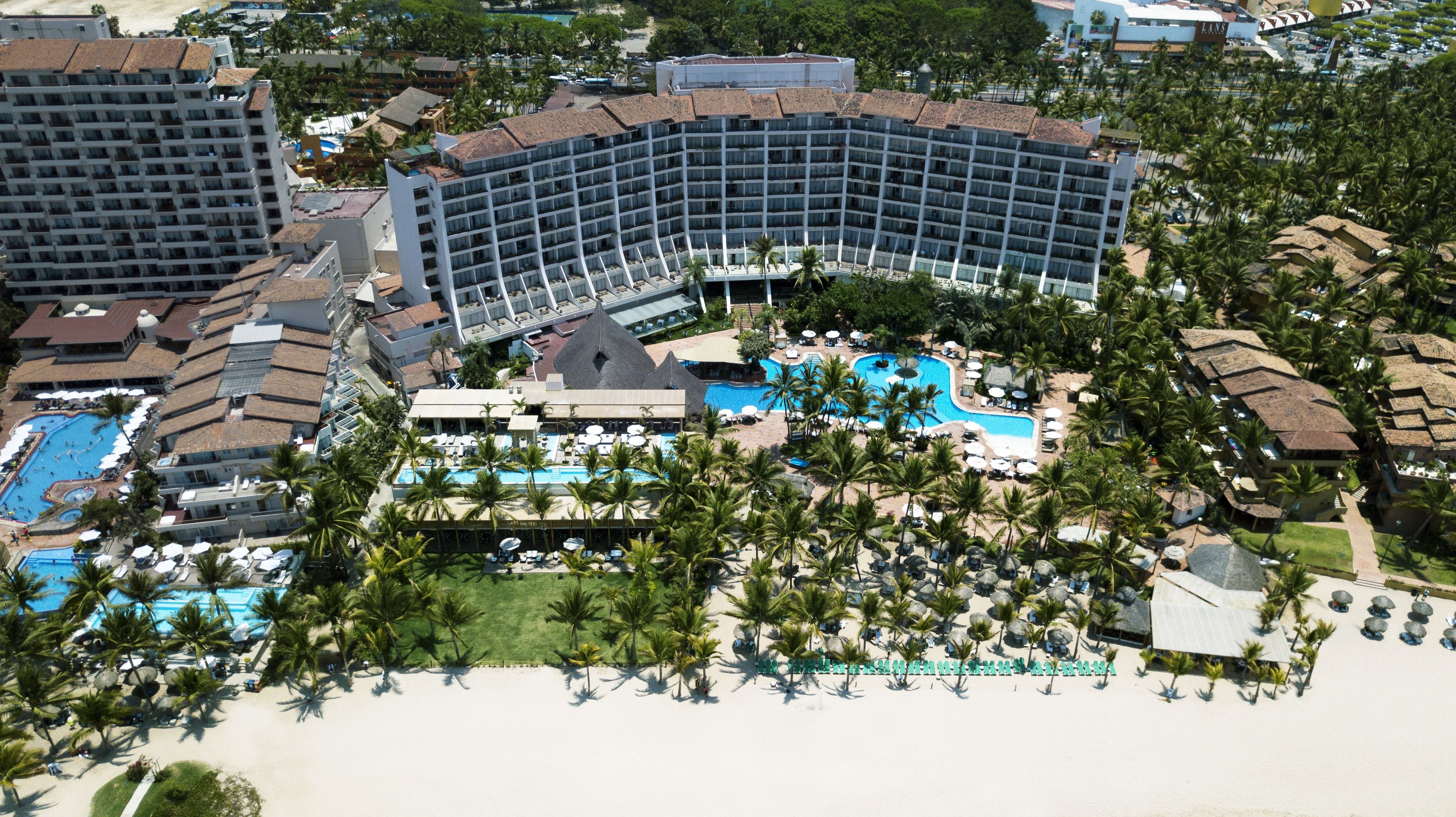 A resort with multiple swimming pools, a large central pool, and a beach area with palm trees.