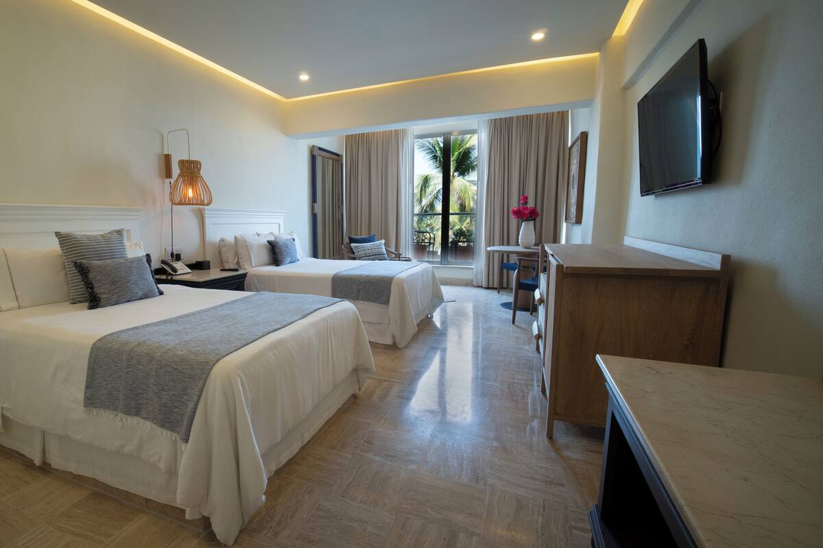 A hotel room with two beds, a desk, a TV, and a window with curtains.