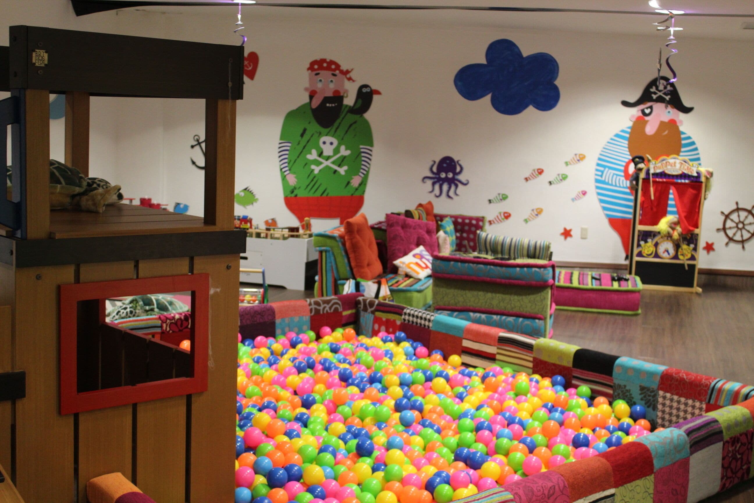 A play area with a ball pit, wooden play structures, and colorful wall decorations.