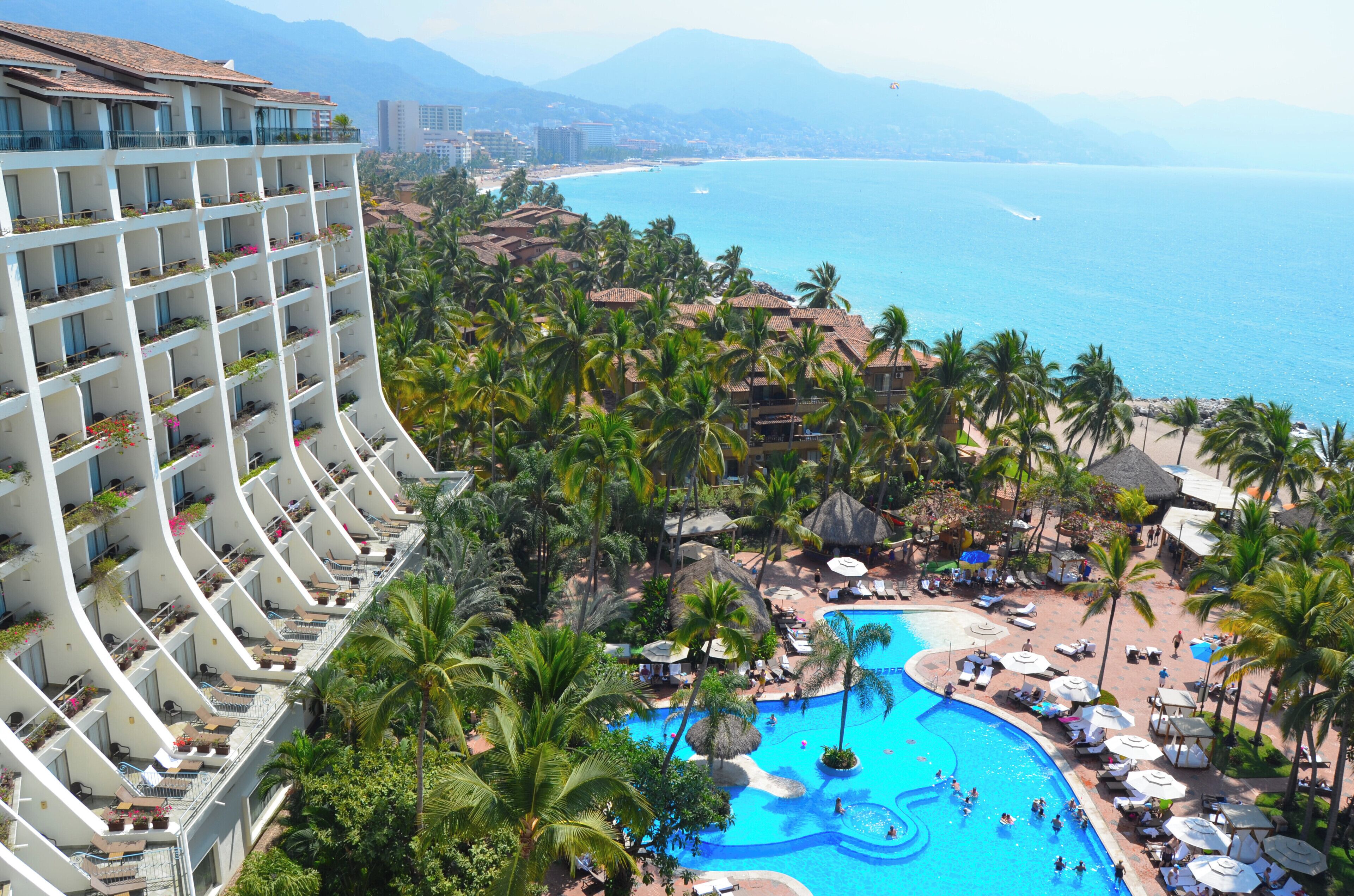 A hotel with a pool, palm trees, and a view of the ocean.