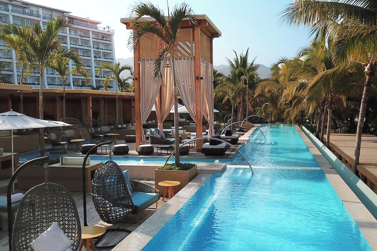 A hotel pool area with lounge chairs, a wooden deck, and palm trees.