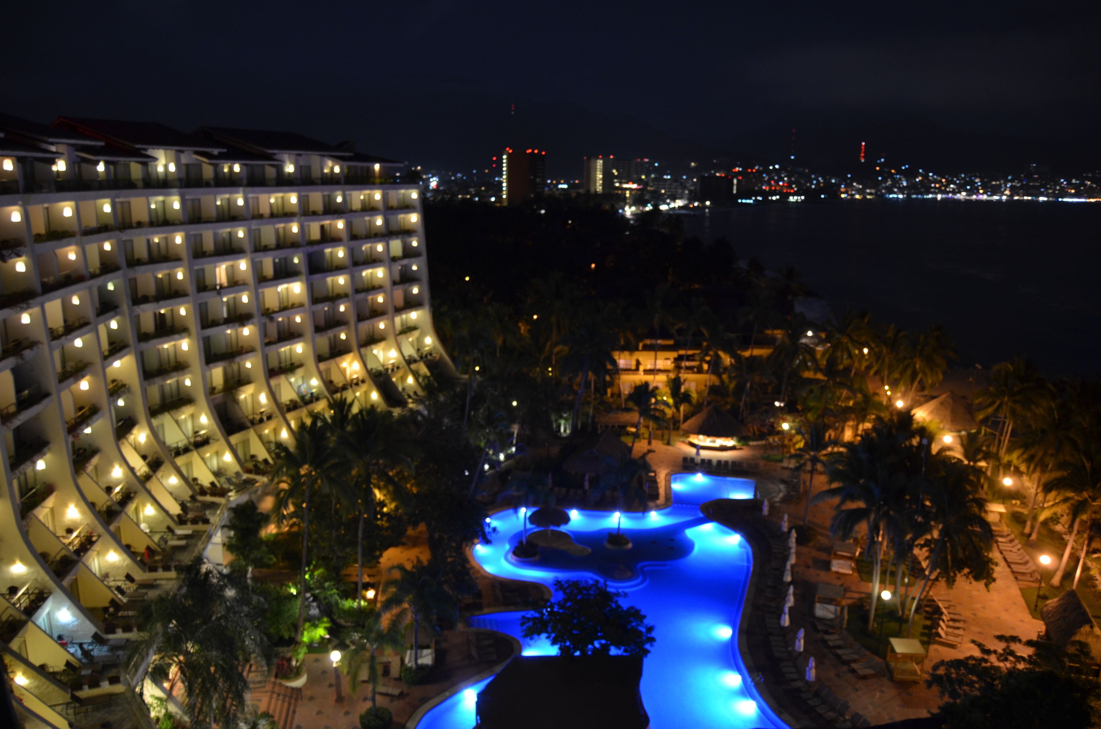 A hotel with multiple floors, a swimming pool, and a view of the city at night.