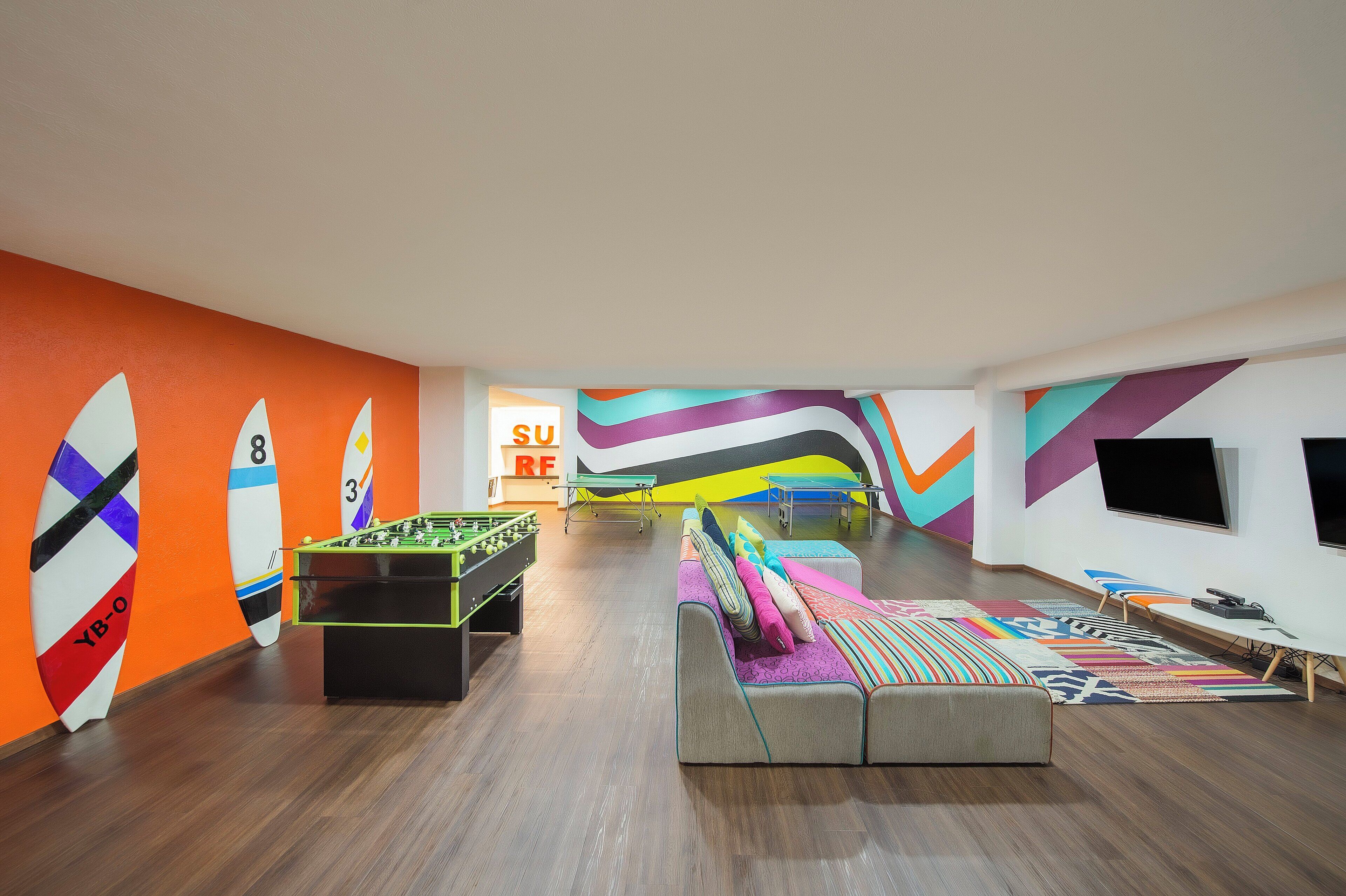 A room with a foosball table, a sofa, and a ping pong table.