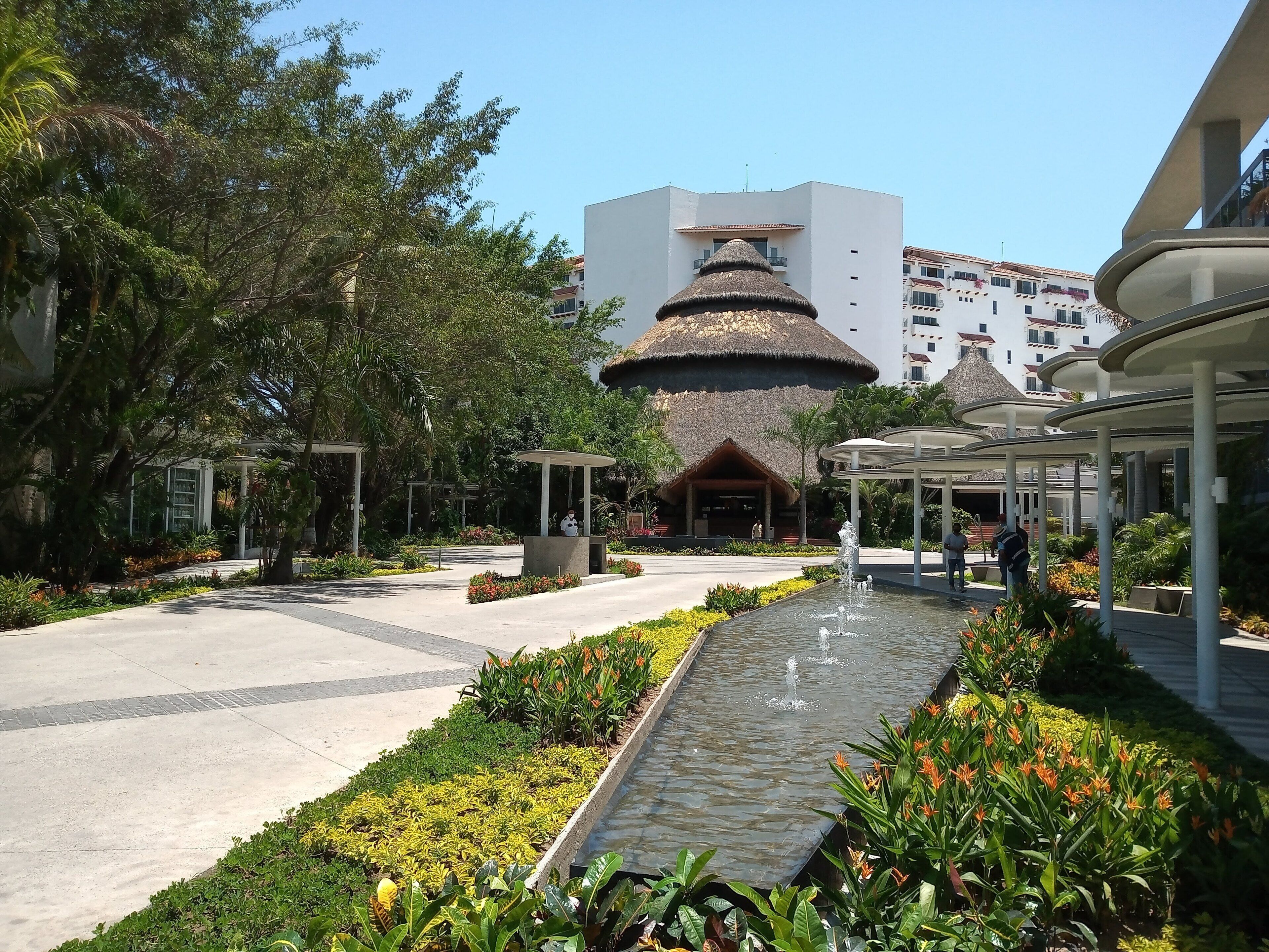 Un resort con una fuente central, una edificación de techo de paja y un paseo techado.