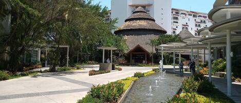 Un resort con una fuente central, una edificación de techo de paja y un paseo techado.