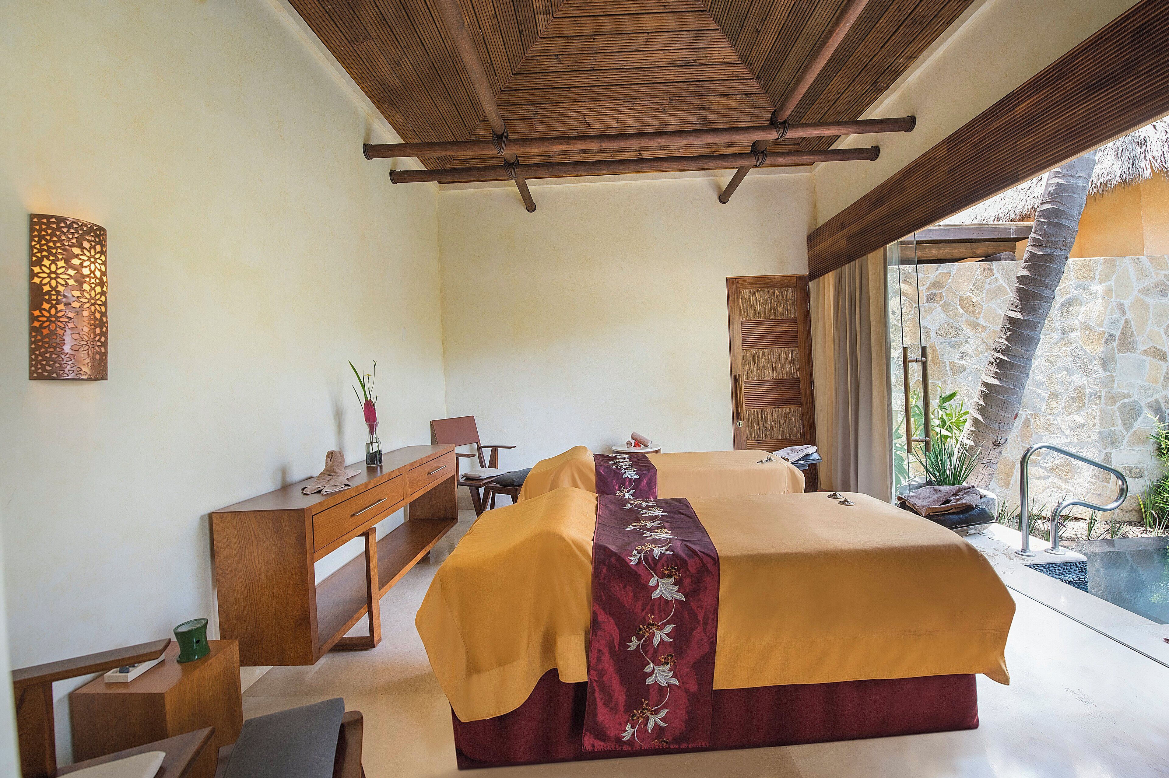 A bedroom with a bed, a desk, and a chair. There is a window with a view of a pool and palm trees.