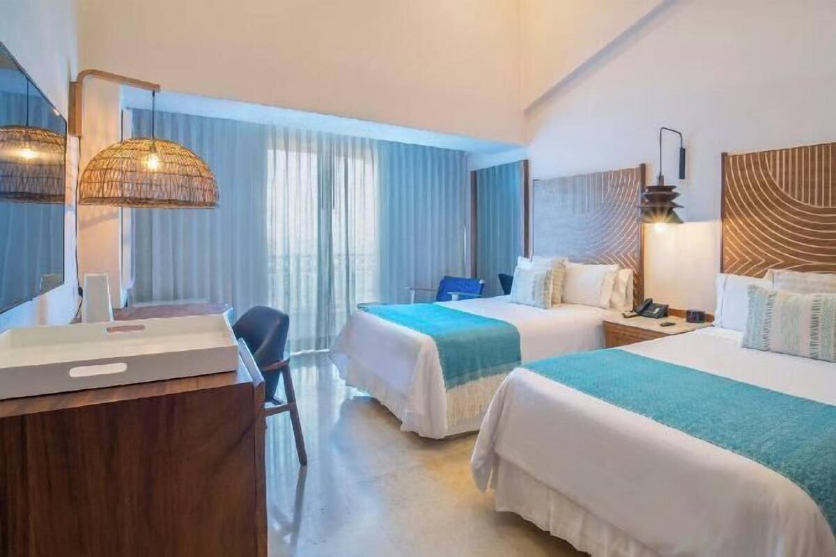 A hotel room with two beds, a desk, a chair, and a large window with curtains.