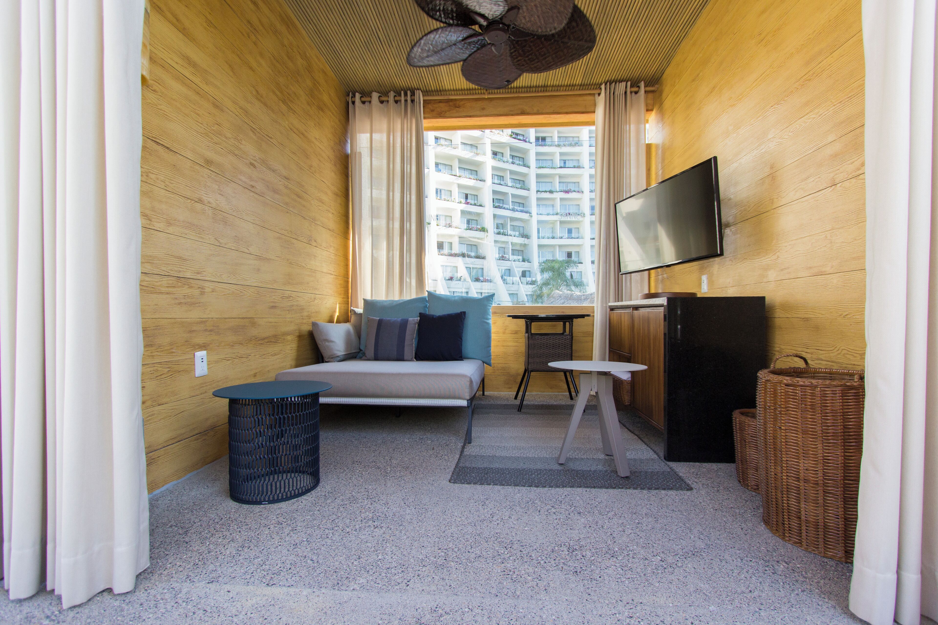 Una habitación pequeña con cama, televisión, mesita y ventana con vista a un edificio de gran altura.