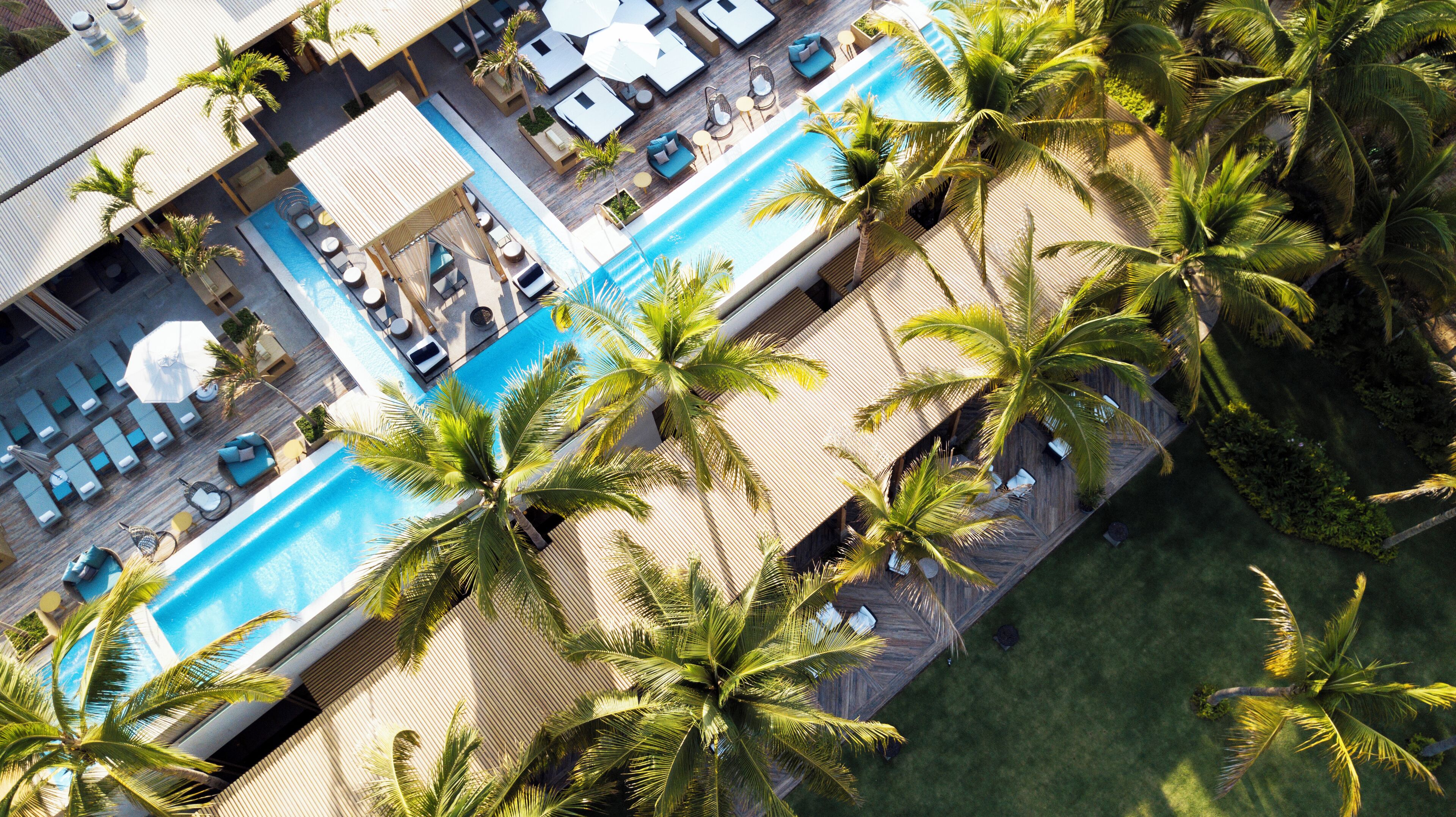 An aerial view of a hotel with a swimming pool surrounded by palm trees and sun loungers.