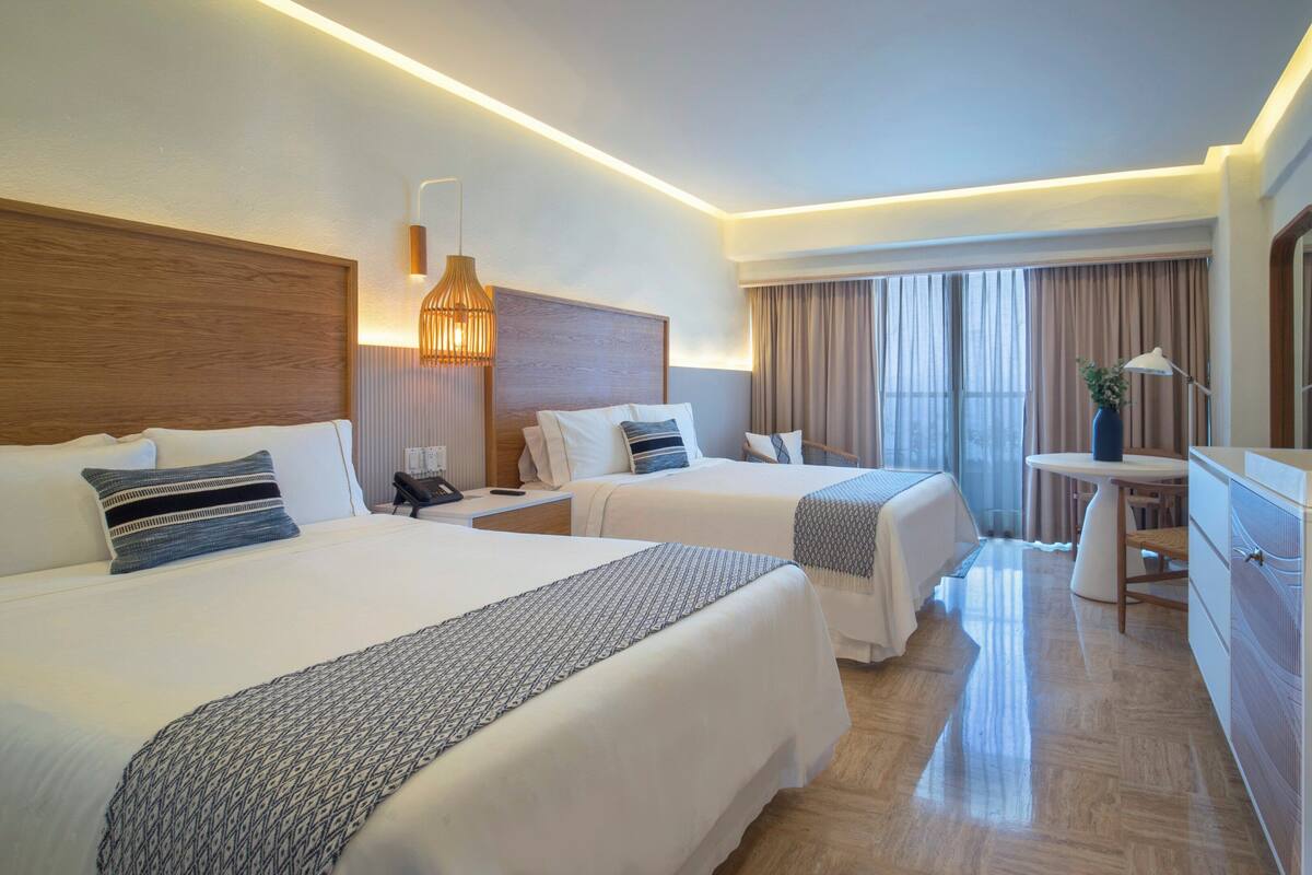 A hotel room with two beds, a desk, a chair, a TV, and a coffee machine.
