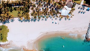 Een overzicht vanuit de lucht van een strand met helder turquoise water, een zandstrand en palmbomen.