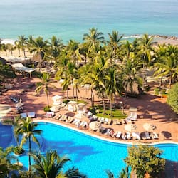 Relax by the serene beachfront pool surrounded by palm trees and sun loungers.