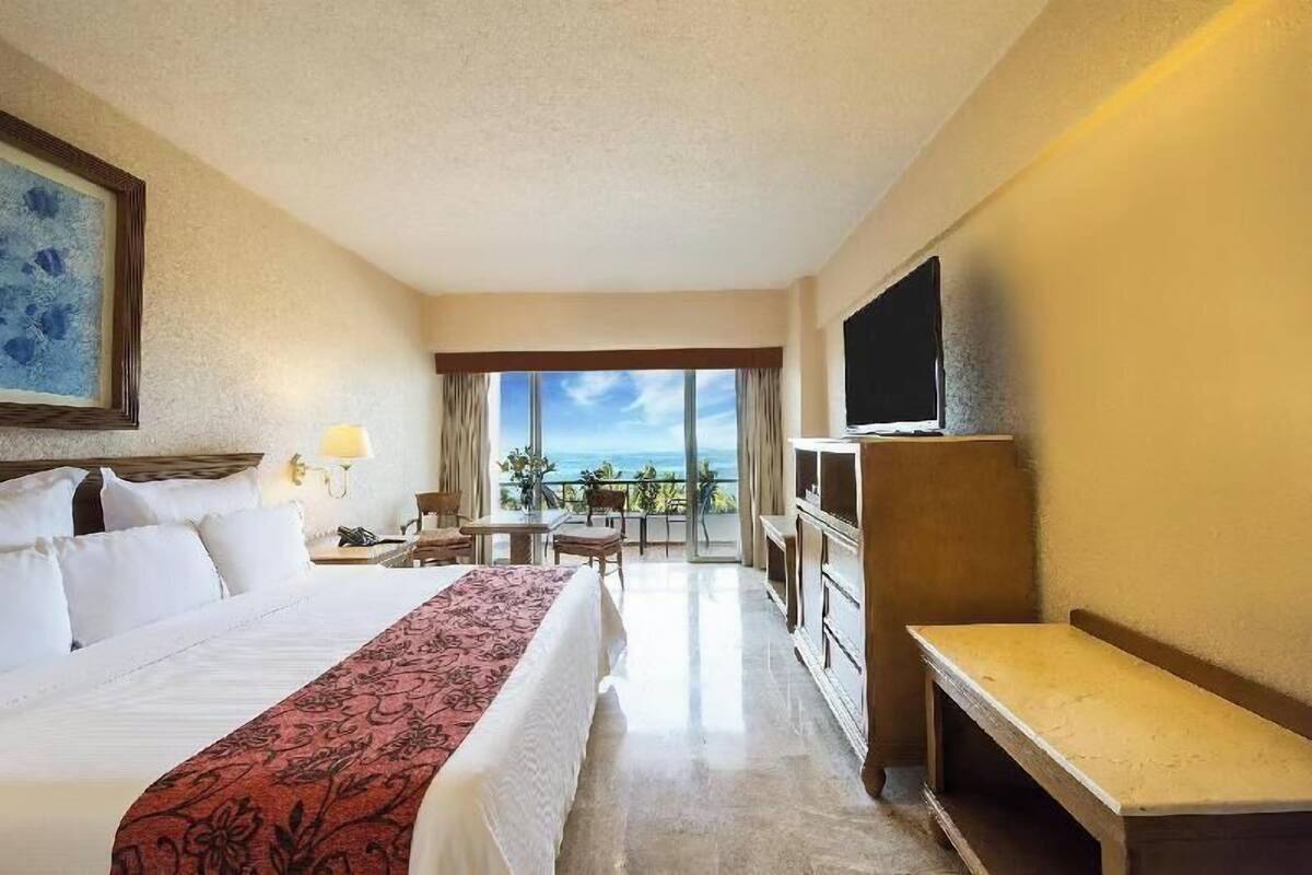 A hotel room with a bed, a TV, a desk, and a balcony with a view.
